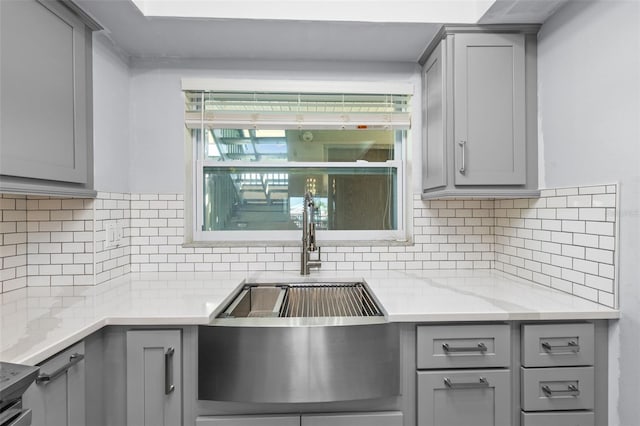 kitchen featuring gray cabinets, backsplash, and light stone countertops