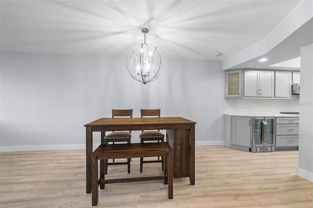 dining room featuring a textured ceiling, light hardwood / wood-style flooring, wine cooler, and an inviting chandelier