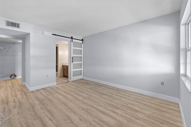 unfurnished bedroom with light wood-type flooring, a textured ceiling, a closet, ensuite bathroom, and a barn door