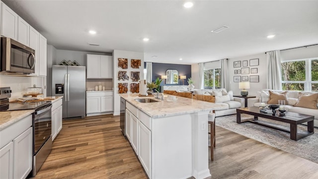 kitchen with an island with sink, hardwood / wood-style floors, stainless steel appliances, and white cabinets