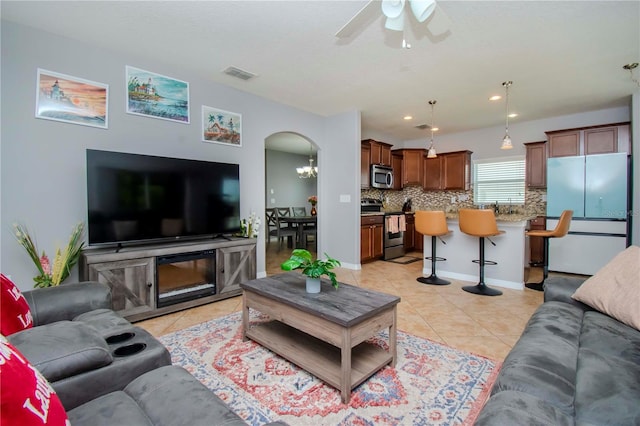 tiled living room with ceiling fan with notable chandelier