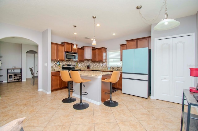 kitchen with a kitchen breakfast bar, light stone counters, a kitchen island, hanging light fixtures, and appliances with stainless steel finishes