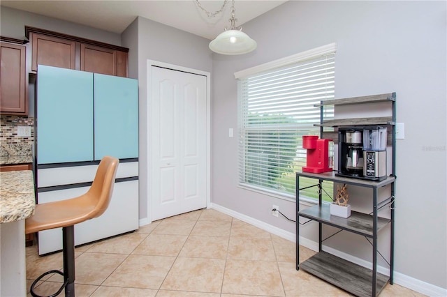 kitchen with white fridge, tasteful backsplash, light tile patterned floors, light stone counters, and hanging light fixtures