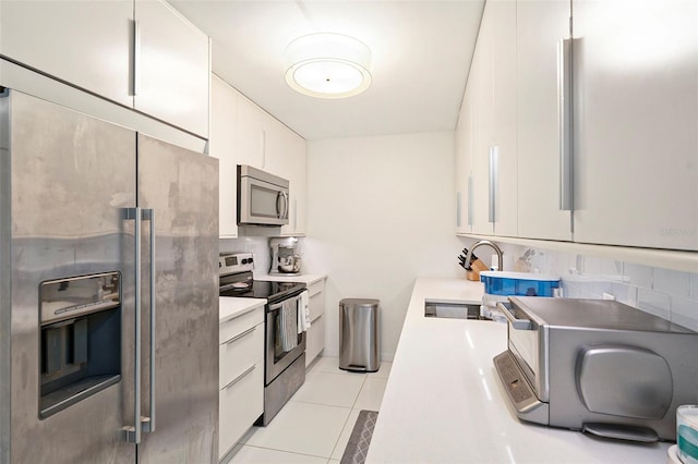 kitchen with light tile patterned floors, backsplash, stainless steel appliances, sink, and white cabinetry