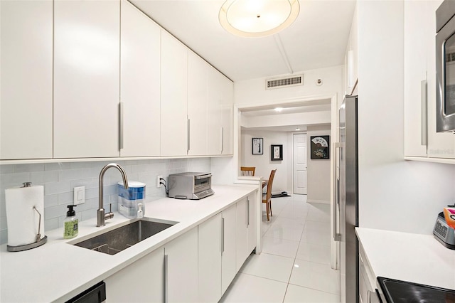 kitchen with stainless steel refrigerator with ice dispenser, tasteful backsplash, sink, white cabinets, and light tile patterned flooring