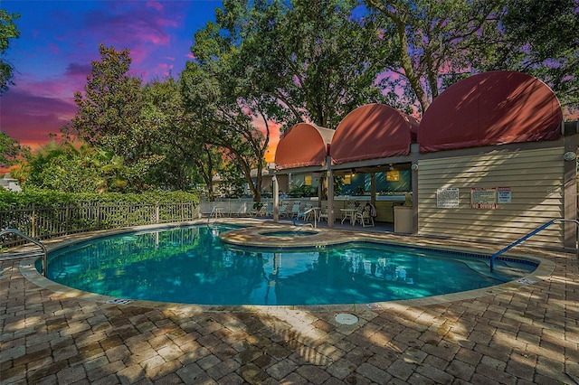 pool at dusk featuring a hot tub and a patio area