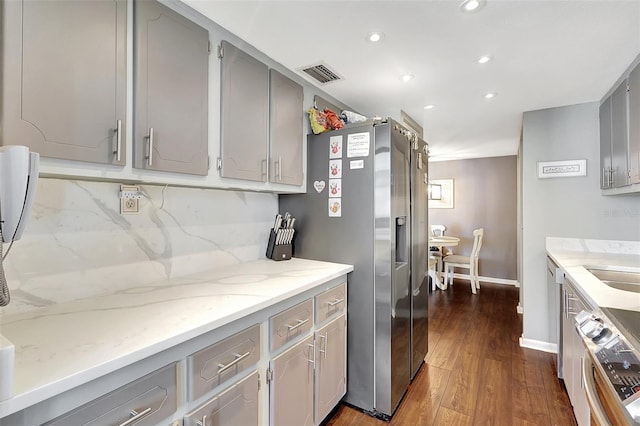 kitchen featuring gray cabinets, light stone counters, dark wood-type flooring, decorative backsplash, and stainless steel appliances