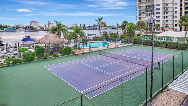 view of tennis court featuring a community pool and a water view