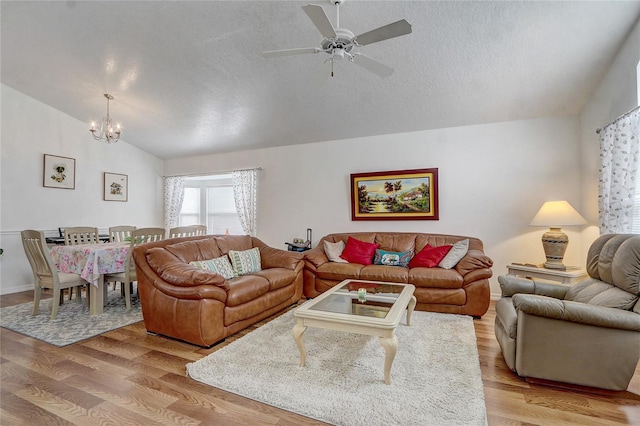 living room with a textured ceiling, light hardwood / wood-style flooring, vaulted ceiling, and ceiling fan with notable chandelier