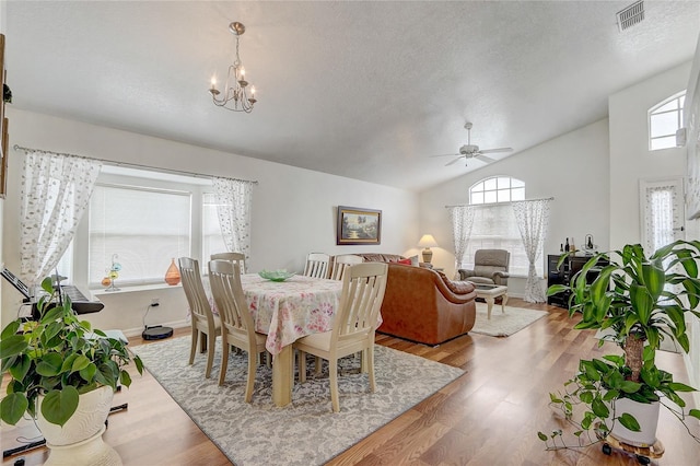 dining room with a textured ceiling, vaulted ceiling, ceiling fan with notable chandelier, and light hardwood / wood-style floors