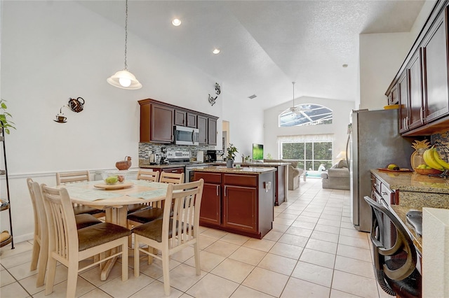 kitchen with appliances with stainless steel finishes, light stone counters, light tile patterned flooring, high vaulted ceiling, and pendant lighting