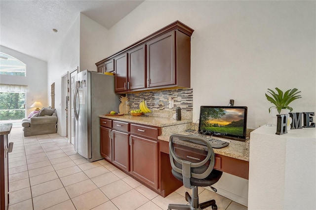 kitchen featuring stainless steel fridge, built in desk, light tile patterned flooring, and tasteful backsplash