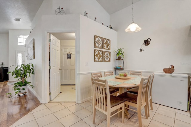 dining room featuring a textured ceiling, high vaulted ceiling, and light tile patterned flooring