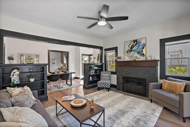 living room with ceiling fan, a fireplace, wood-type flooring, and a textured ceiling