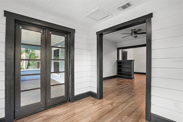 interior space with wood walls, wood-type flooring, and french doors