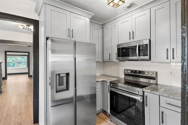 kitchen with stainless steel appliances, tasteful backsplash, light stone counters, light hardwood / wood-style flooring, and a textured ceiling