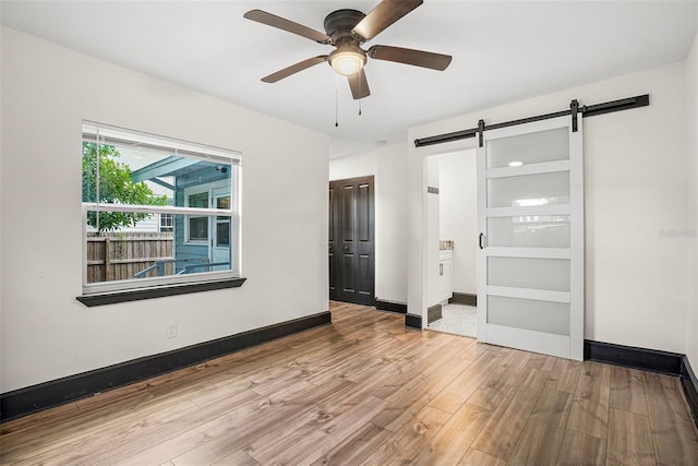 unfurnished bedroom with ceiling fan, a barn door, and light hardwood / wood-style floors