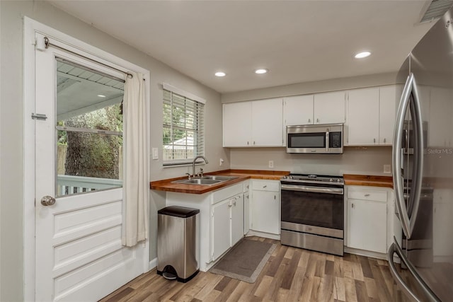 kitchen with white cabinets, a sink, wooden counters, light wood finished floors, and stainless steel appliances