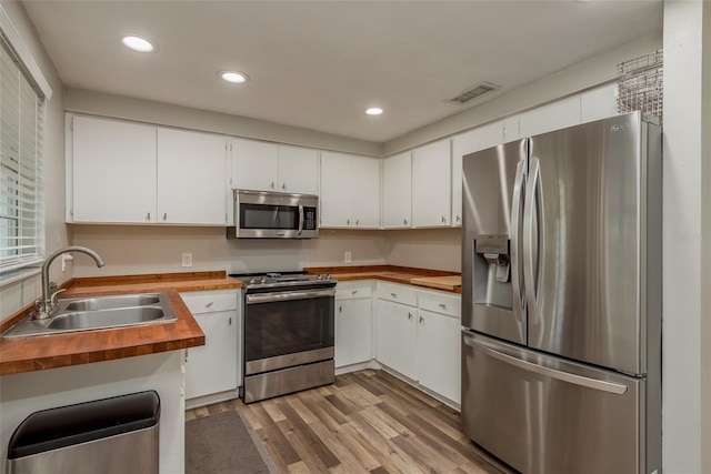 kitchen with butcher block countertops, visible vents, stainless steel appliances, light wood finished floors, and a sink