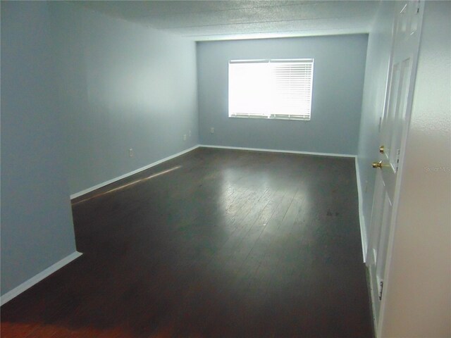 spare room with dark wood-type flooring and baseboards