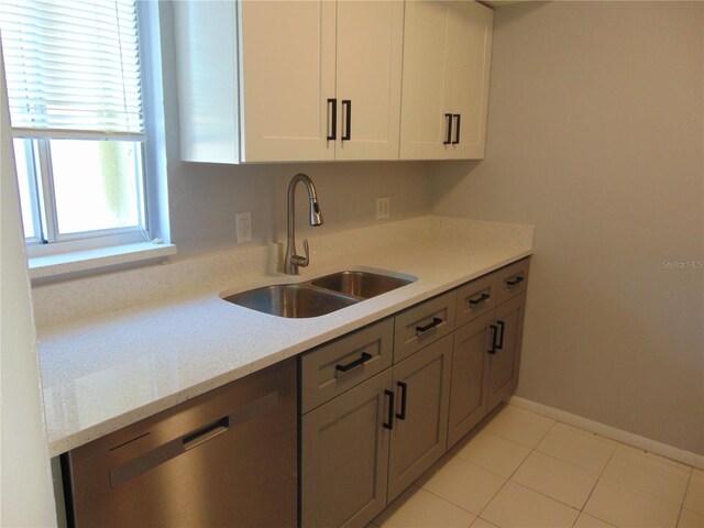 kitchen featuring light tile patterned floors, baseboards, dishwasher, white cabinetry, and a sink