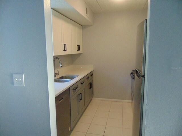 kitchen with light tile patterned floors, dishwashing machine, a sink, white cabinets, and light countertops