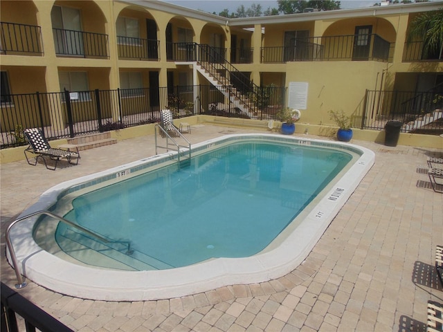 community pool with a patio area, stairs, and fence