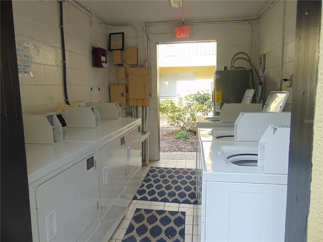 clothes washing area featuring light tile patterned floors, water heater, independent washer and dryer, electric panel, and concrete block wall