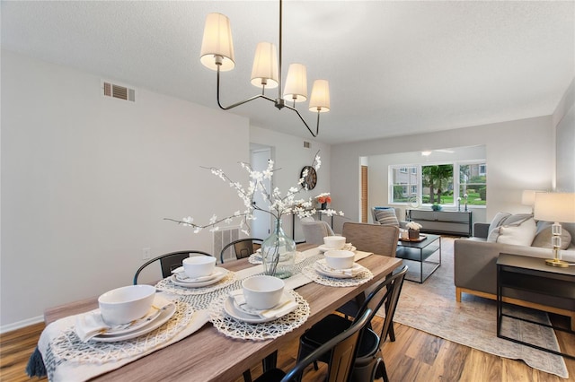 dining space featuring wood-type flooring, a chandelier, and a textured ceiling