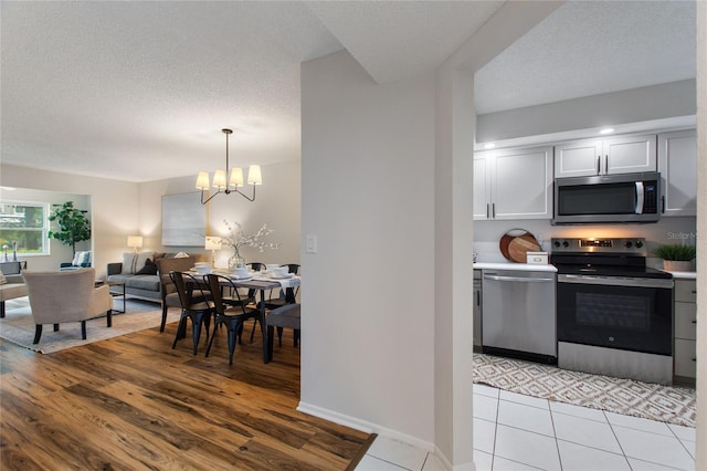 kitchen with a textured ceiling, decorative light fixtures, appliances with stainless steel finishes, a chandelier, and light wood-type flooring