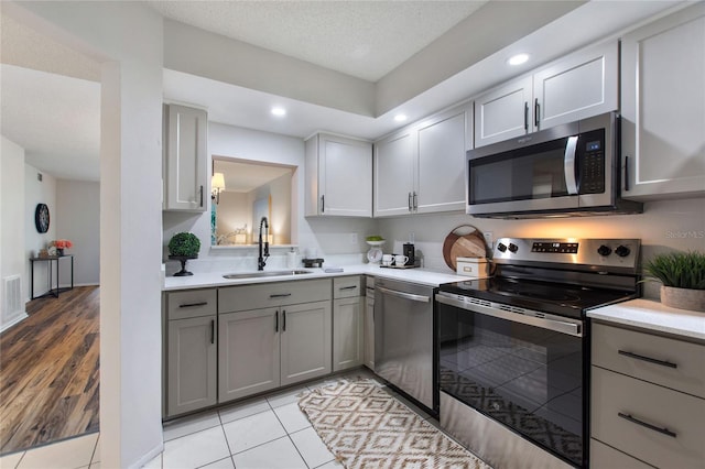 kitchen with gray cabinets, a textured ceiling, sink, appliances with stainless steel finishes, and light tile patterned flooring