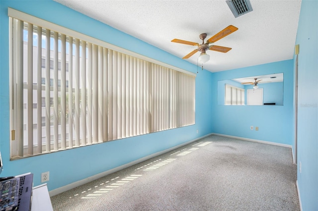 unfurnished room with a wealth of natural light, ceiling fan, carpet floors, and a textured ceiling