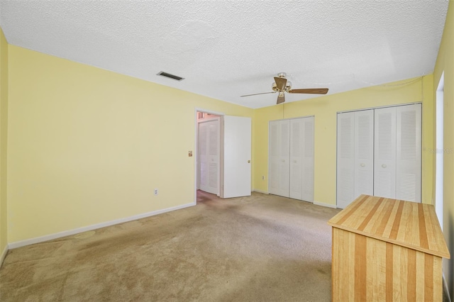 unfurnished bedroom with two closets, ceiling fan, light colored carpet, and a textured ceiling