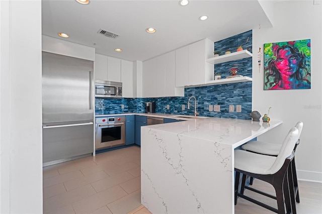 kitchen featuring light stone countertops, appliances with stainless steel finishes, a kitchen bar, kitchen peninsula, and sink