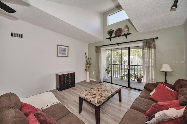 living room with high vaulted ceiling, a healthy amount of sunlight, a textured ceiling, and light hardwood / wood-style flooring