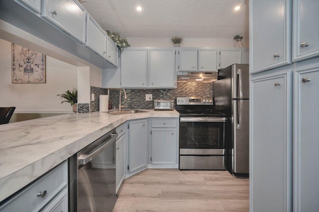 kitchen with appliances with stainless steel finishes, sink, backsplash, a textured ceiling, and light hardwood / wood-style flooring