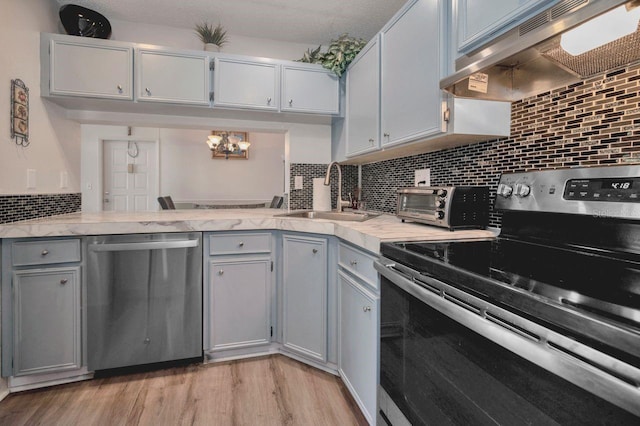 kitchen featuring wall chimney range hood, sink, light hardwood / wood-style floors, stainless steel appliances, and gray cabinets