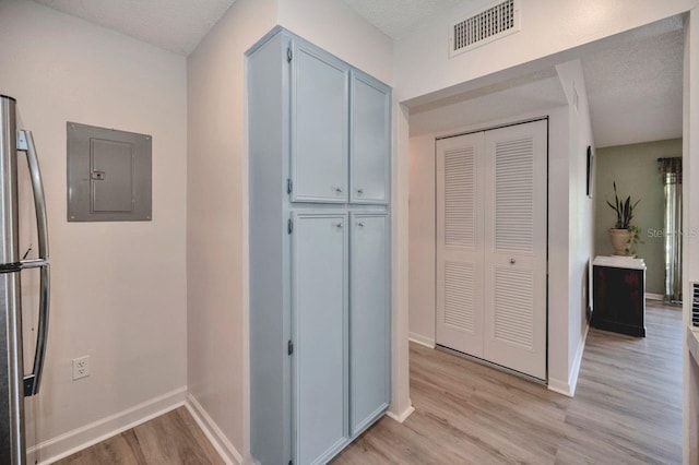 hall featuring light hardwood / wood-style floors, a textured ceiling, and electric panel