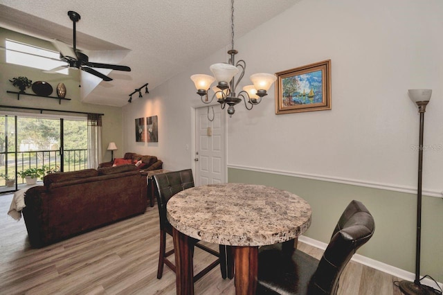 dining room with vaulted ceiling, a textured ceiling, wood-type flooring, and ceiling fan with notable chandelier