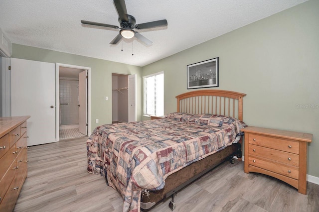 bedroom with a closet, a spacious closet, light wood-type flooring, a textured ceiling, and ceiling fan