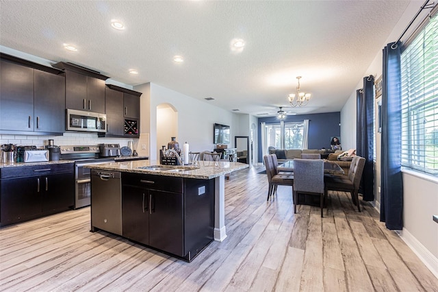 kitchen with appliances with stainless steel finishes, plenty of natural light, light hardwood / wood-style floors, sink, and a center island with sink