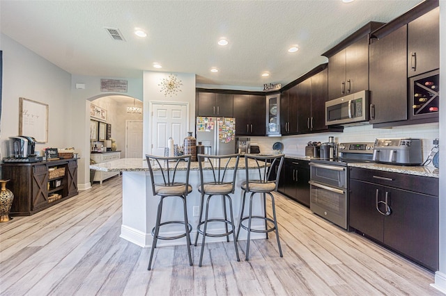 kitchen featuring stainless steel appliances, light hardwood / wood-style floors, dark brown cabinets, a center island with sink, and a textured ceiling