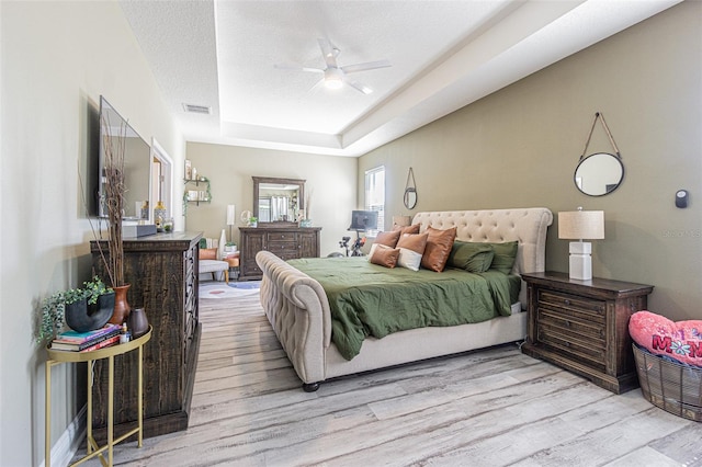 bedroom with a textured ceiling, a raised ceiling, ceiling fan, and light hardwood / wood-style floors