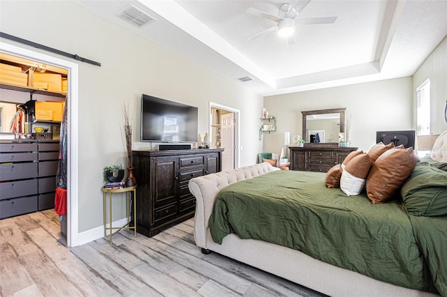 bedroom featuring light wood-type flooring, a textured ceiling, ceiling fan, a closet, and a raised ceiling