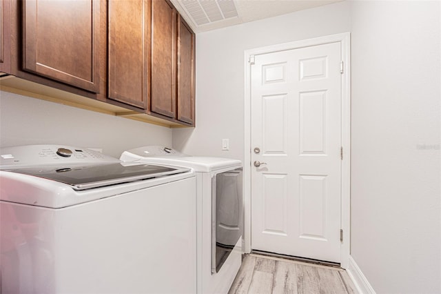 clothes washing area with cabinets, separate washer and dryer, and light wood-type flooring