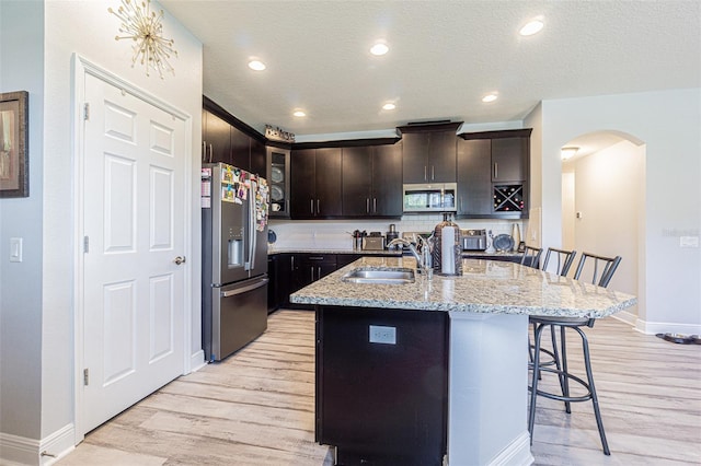 kitchen with a textured ceiling, a center island with sink, appliances with stainless steel finishes, a kitchen bar, and sink