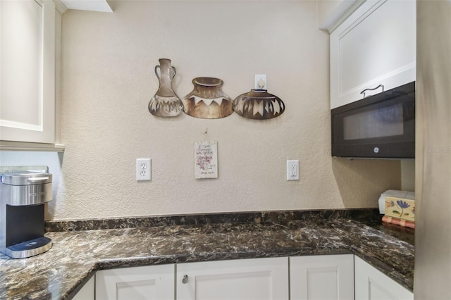 interior details featuring white cabinets, dark stone countertops, and black microwave