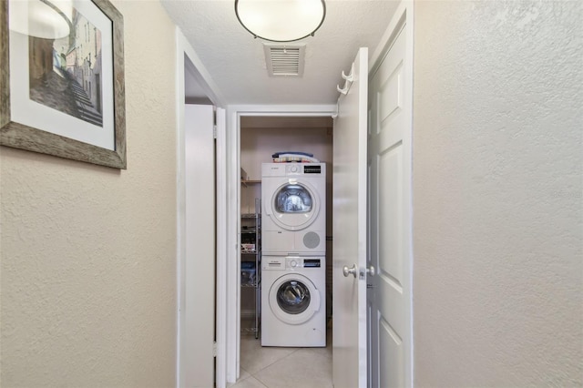 clothes washing area with stacked washer and dryer, a textured ceiling, and light tile patterned flooring