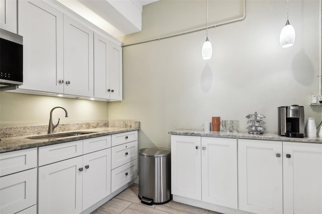 kitchen featuring a sink, stainless steel microwave, and white cabinetry