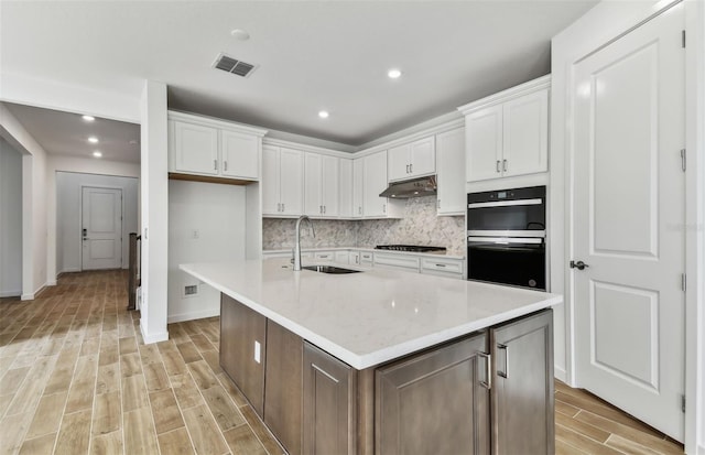 kitchen with white cabinets, a center island with sink, sink, and double oven